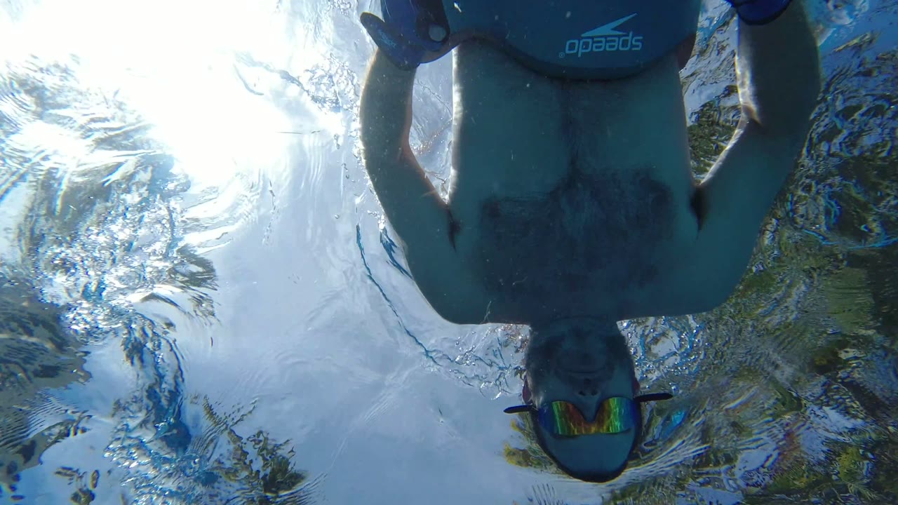 Underwater view of a swimmer wearing goggles and a float belt above the camera.