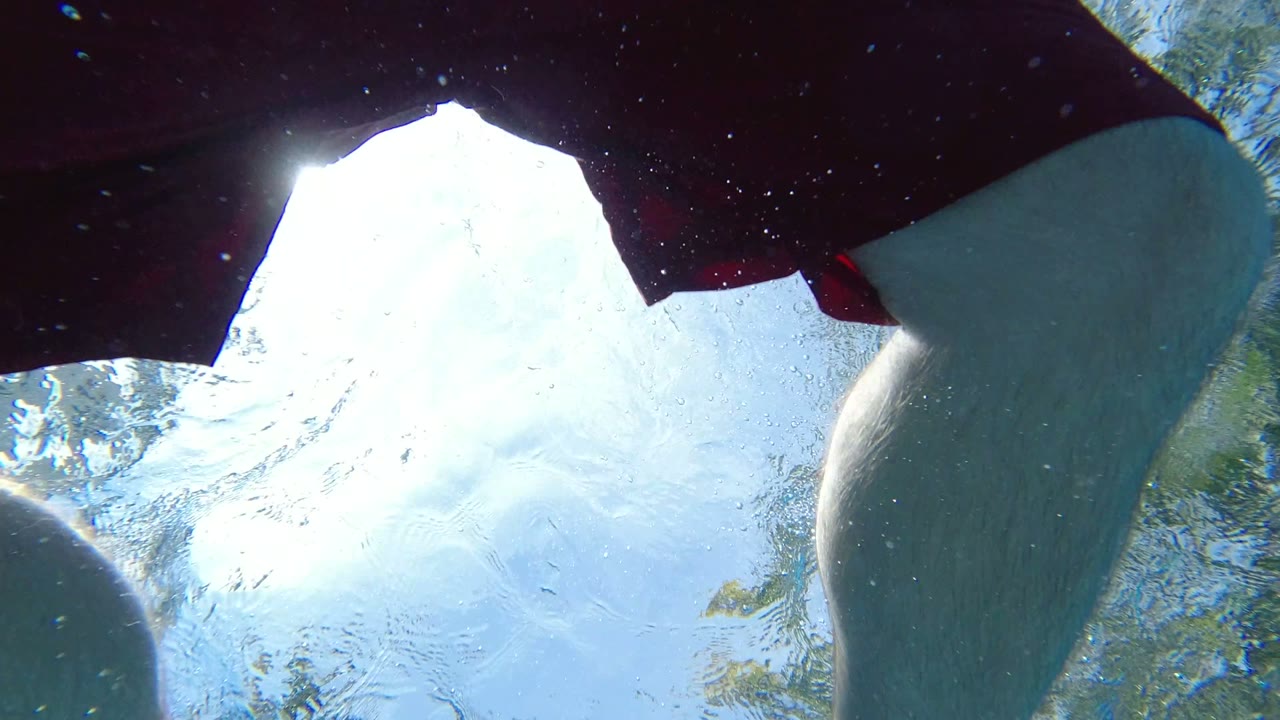 Underwater Los Cabos pool frame with the swimmer's legs and red trunks crossing the top of the image above rippled blue water.
