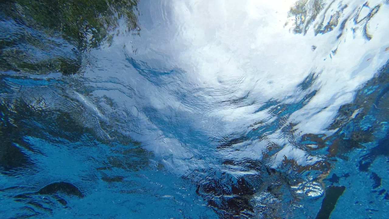 Blue water surface in Los Cabos, Mexico with broad white sky reflections, darker shadowed patches, and no visible people.