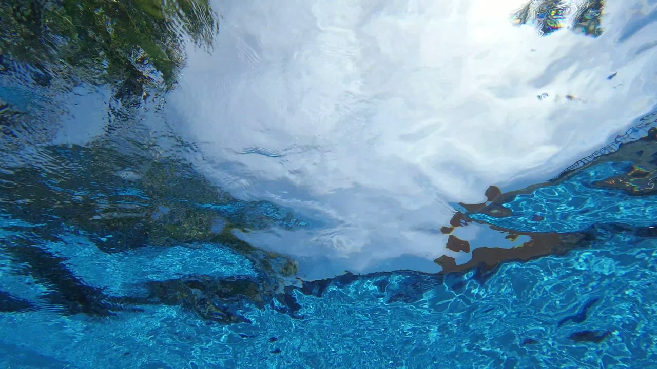 Rippled blue pool water shows a broad pale sky reflection and darker tree reflections near the upper edge, with no visible people.
