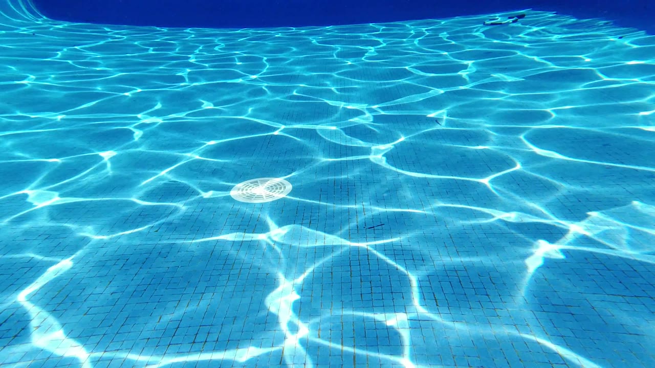 Blue swimming pool floor with bright sun reflections and a round drain cover.