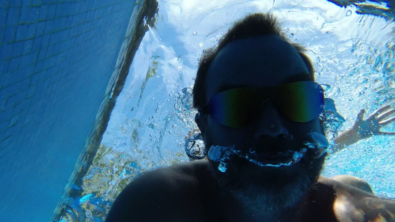 Underwater close-up of a man wearing mirrored swim goggles in a pool.