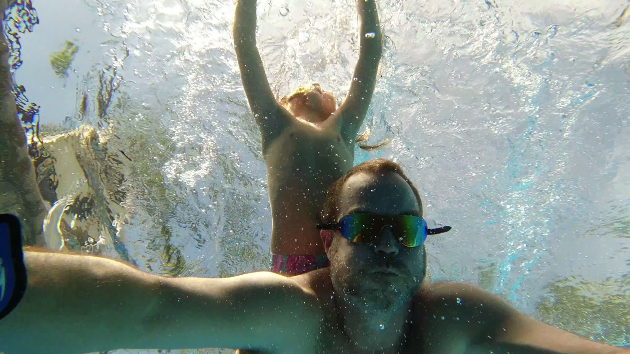 Man in goggles swimming underwater with child behind him