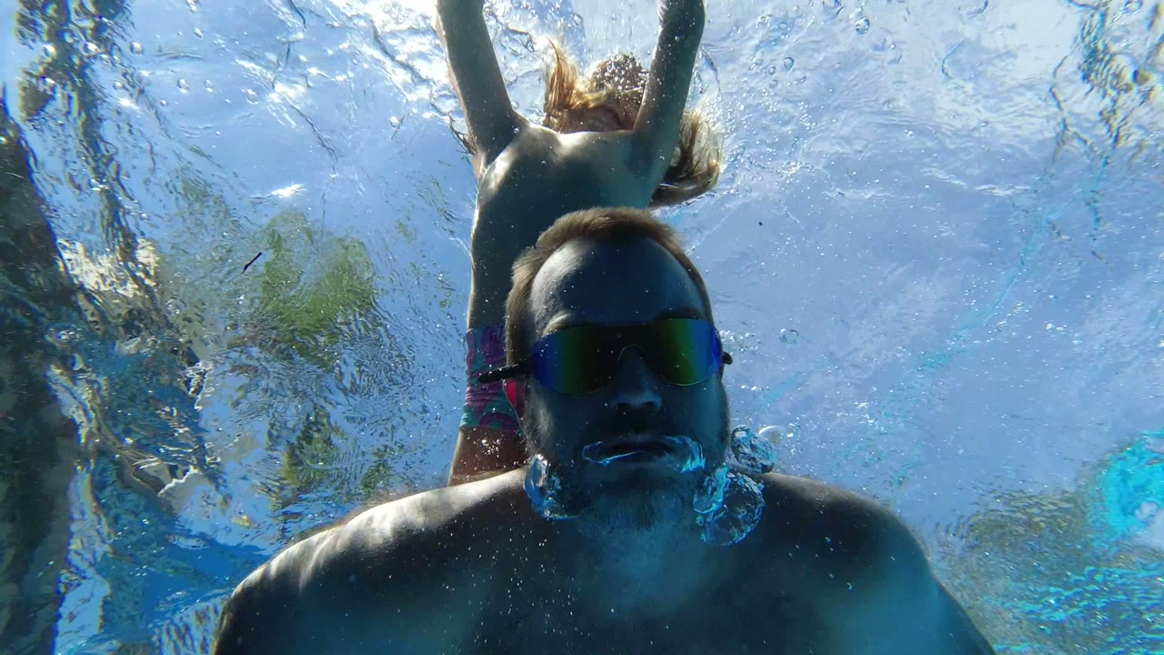 In Los Cabos, Mexico, the man faces the submerged camera from close range while the child's head, arms, and hair appear above him through rippled blue water.