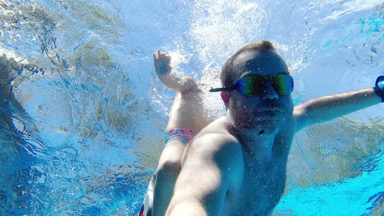 Goggled man underwater near a girl in blue pool water.