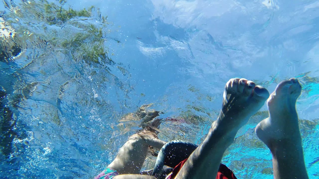 Underwater frame in Los Cabos, Mexico, with a child near the center-left and an adult partly visible at the lower right beneath shimmering pool ripples.