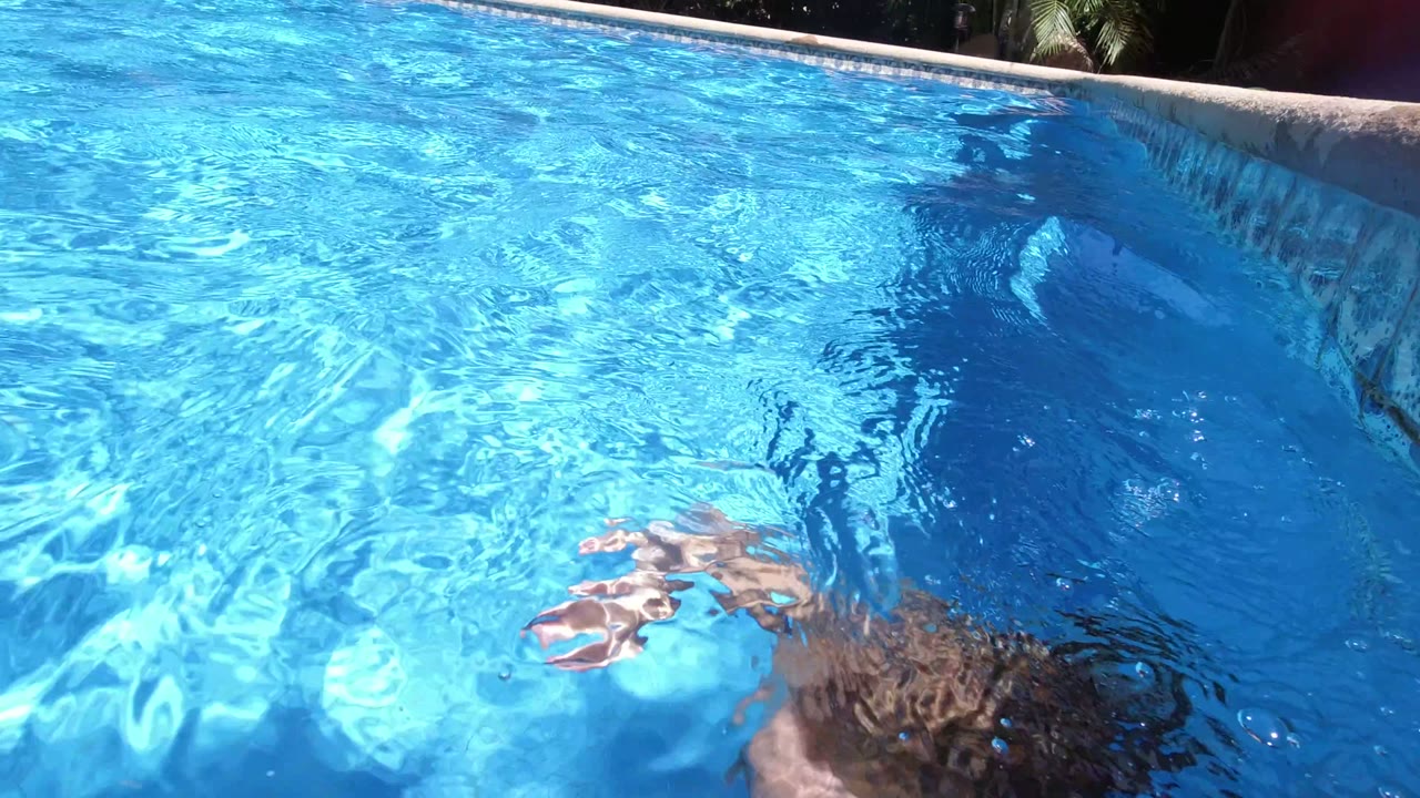At 0:00 in Los Cabos, Mexico, a child is mostly underwater in a bright blue pool, with one hand near the surface and the pool edge visible above.