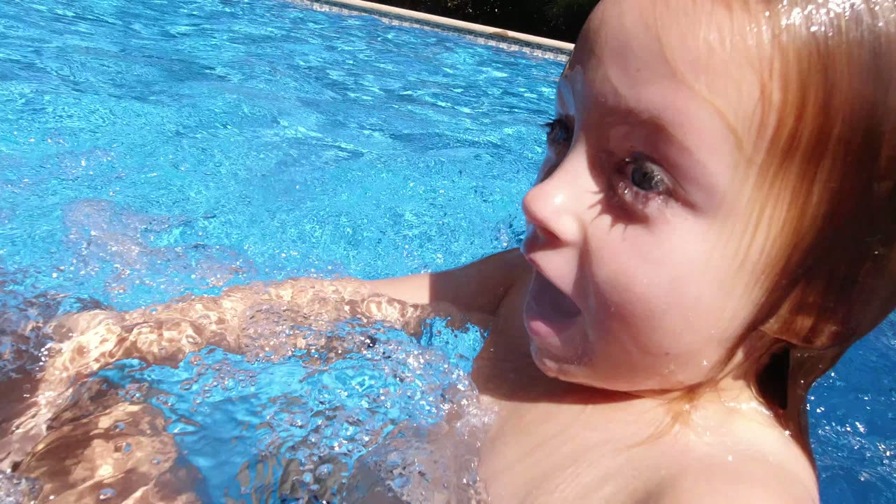At 0:01 in Los Cabos, Mexico, a young blond child surfaces in the pool, face turned sideways, with one arm pushing through rippling blue water.