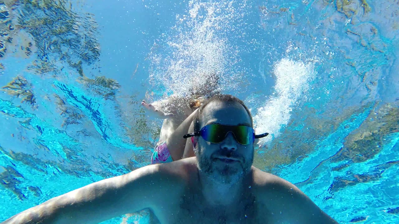 At 0:00, an adult wearing reflective goggles swims close to the underwater camera in a Los Cabos pool, with another swimmer partly visible behind him.