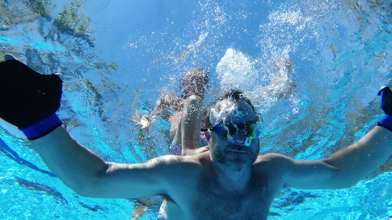 Adult swimmer underwater with raised gloved hands and bubbles.