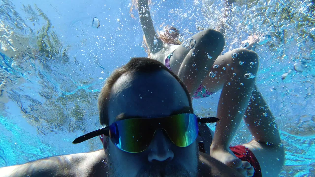 Man in swim goggles underwater with a child above him.