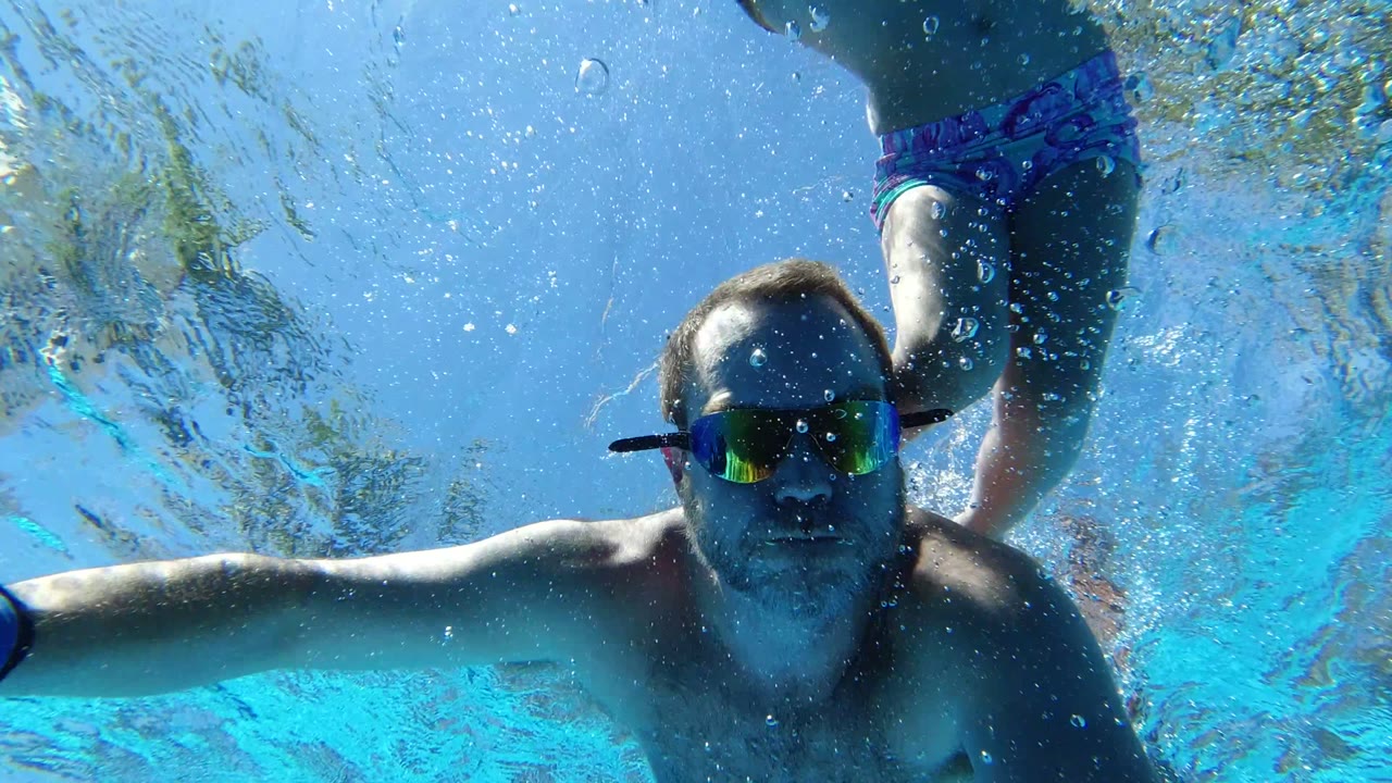 In Los Cabos, Mexico, the man faces the camera underwater with both arms extended while the child in patterned swimwear is partly visible above him.