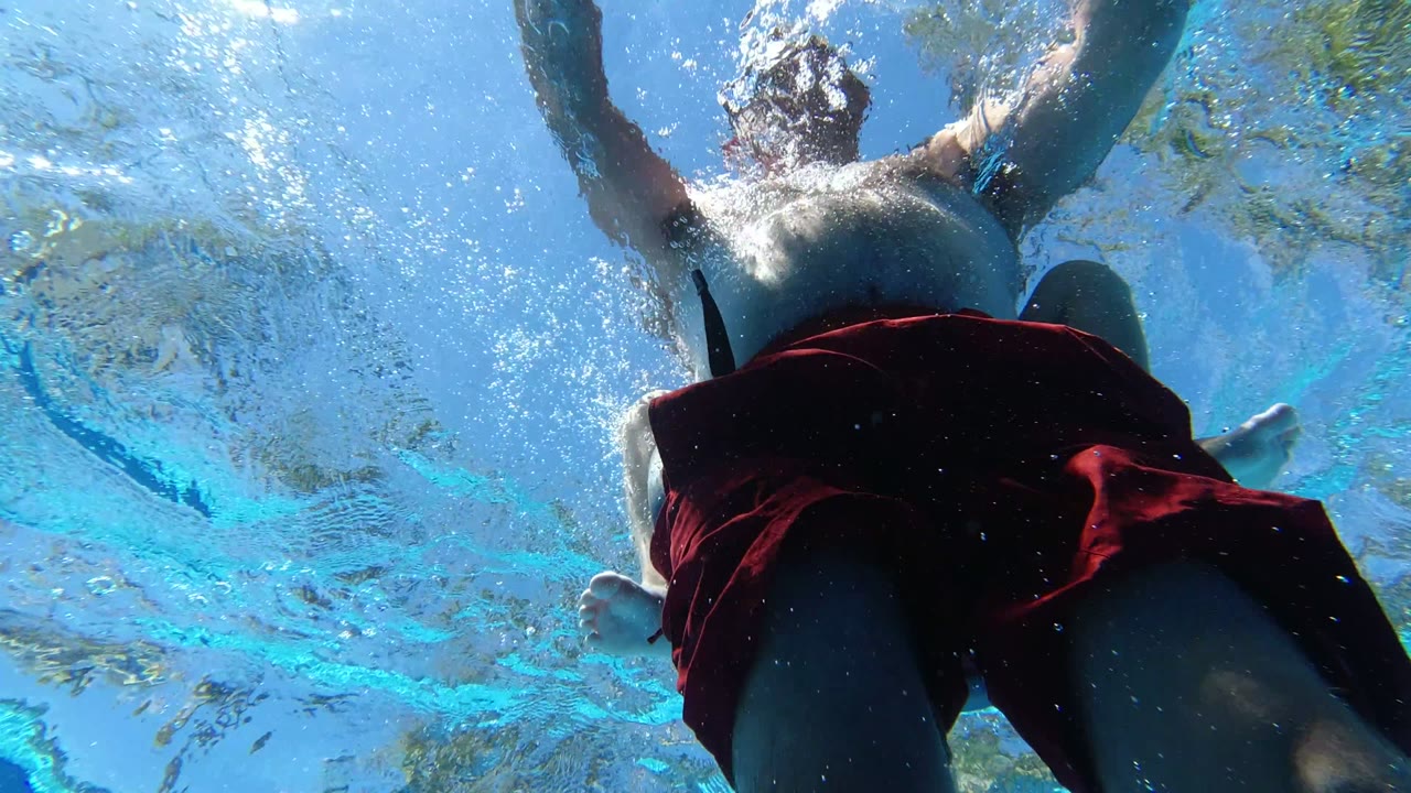 Underwater view of a man in red swim trunks paddling above the camera.