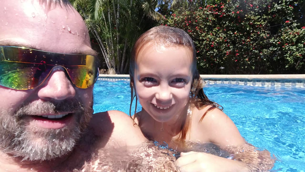 The adult man and child remain close together in the Los Cabos pool, with the child centered and wet hair pulled back beside the blue water.