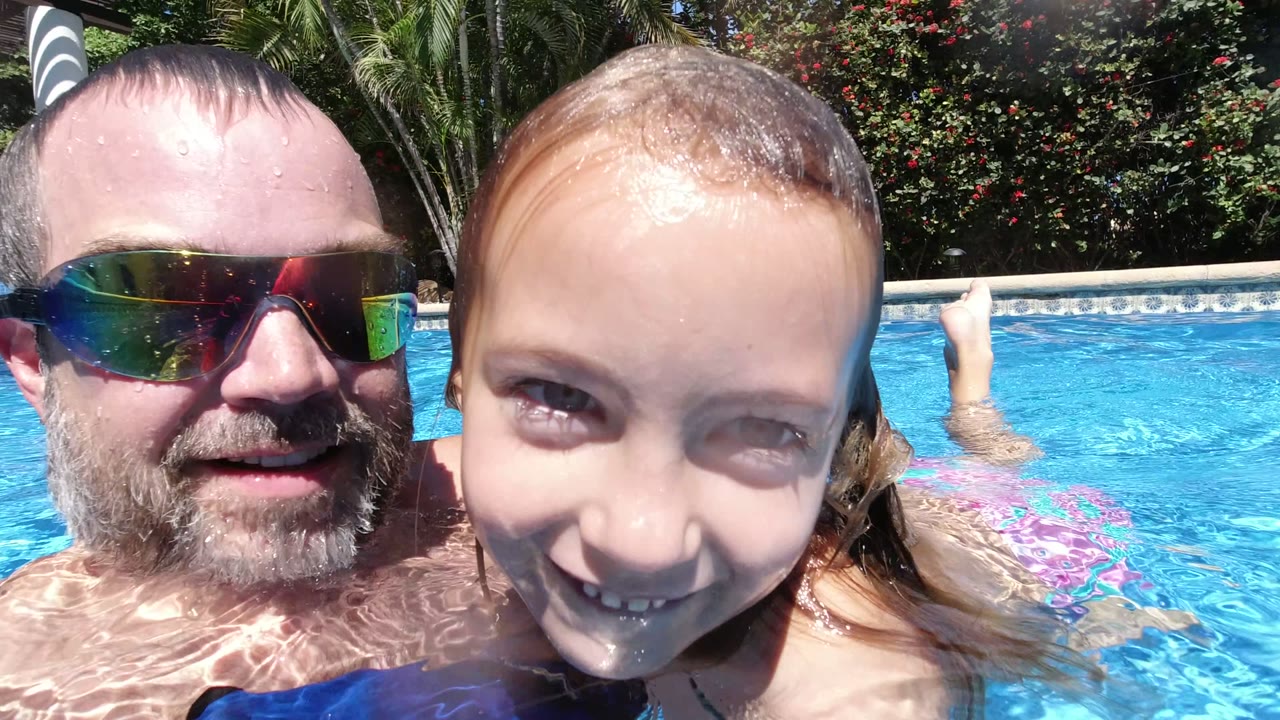Adult man and young girl close to the camera in a sunny swimming pool.