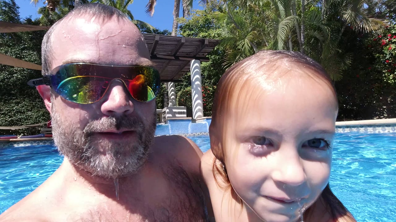 Father and young girl close to camera in a blue swimming pool.