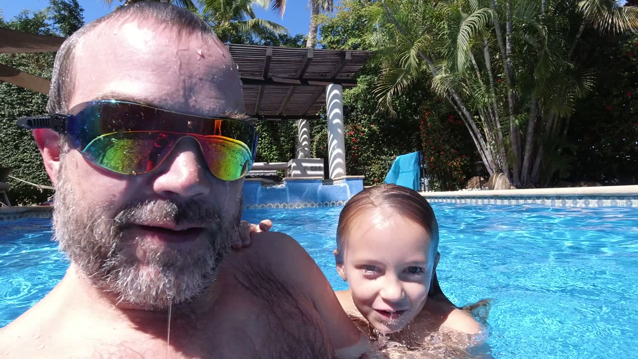 Man in mirrored sunglasses and child at the surface of a swimming pool.