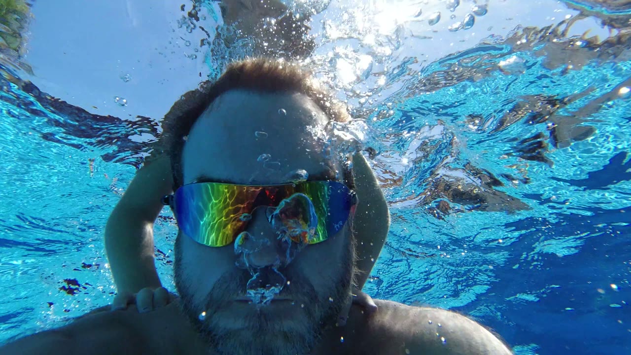 Man in mirrored swim goggles underwater with blue water and bubbles