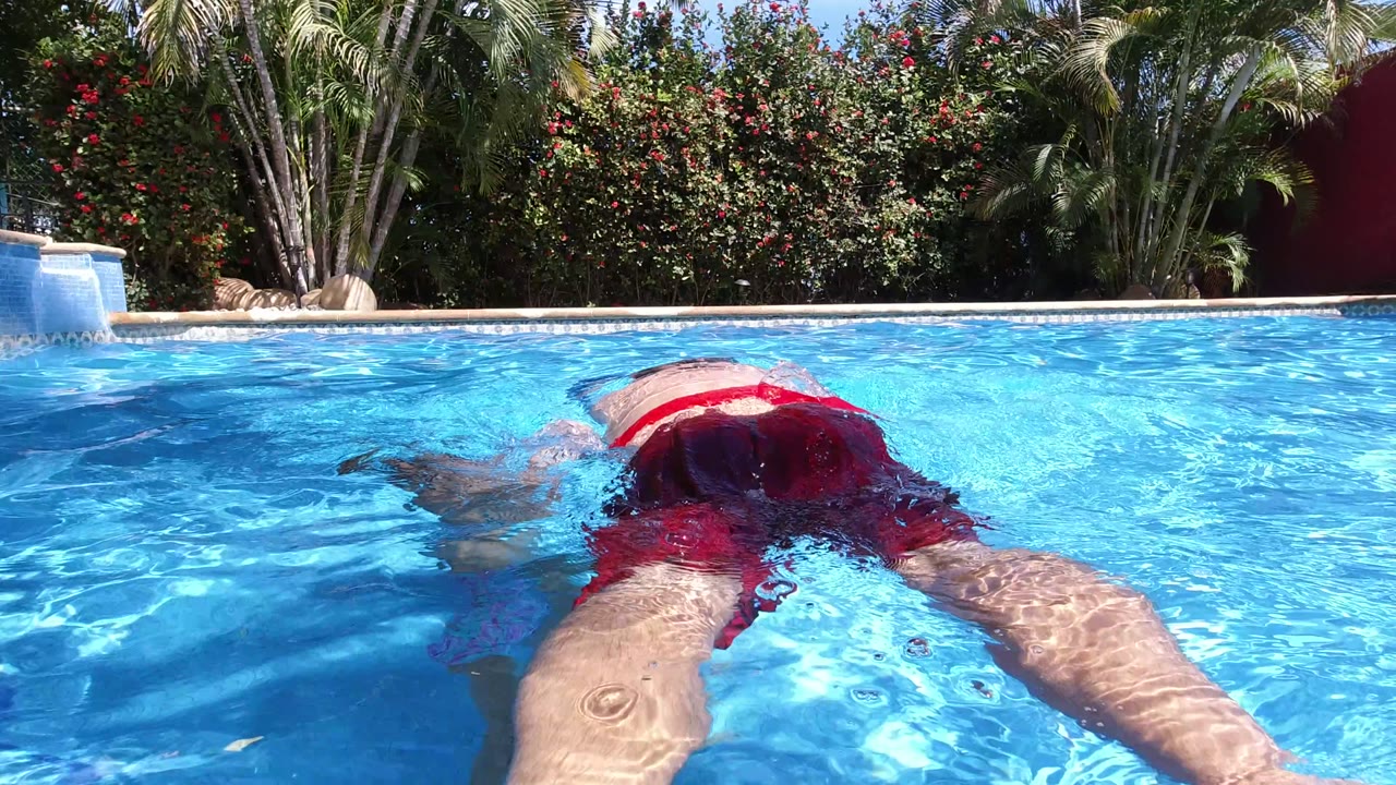 Adult man in red swim trunks floating face down in a bright blue pool.