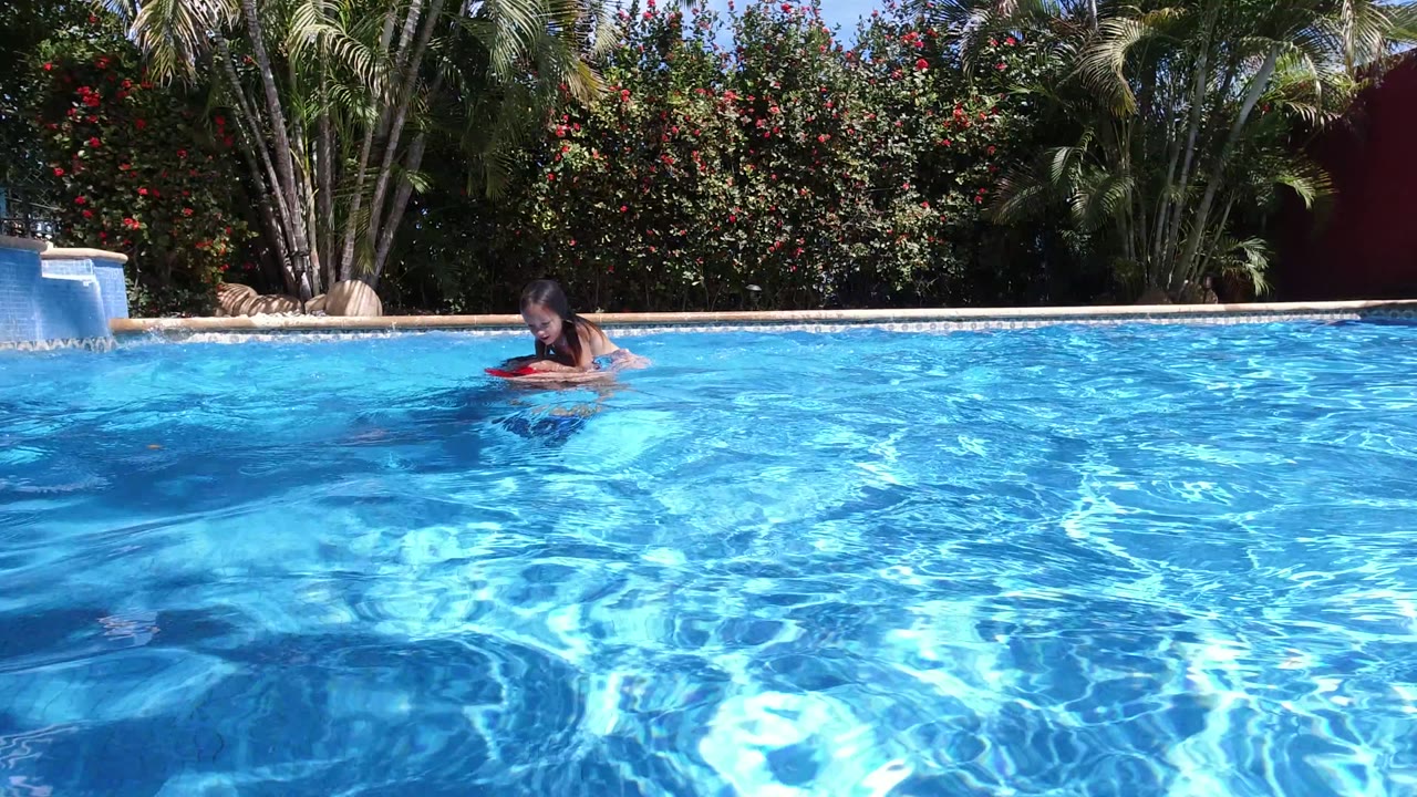 Young girl floating near the edge of a bright blue swimming pool.