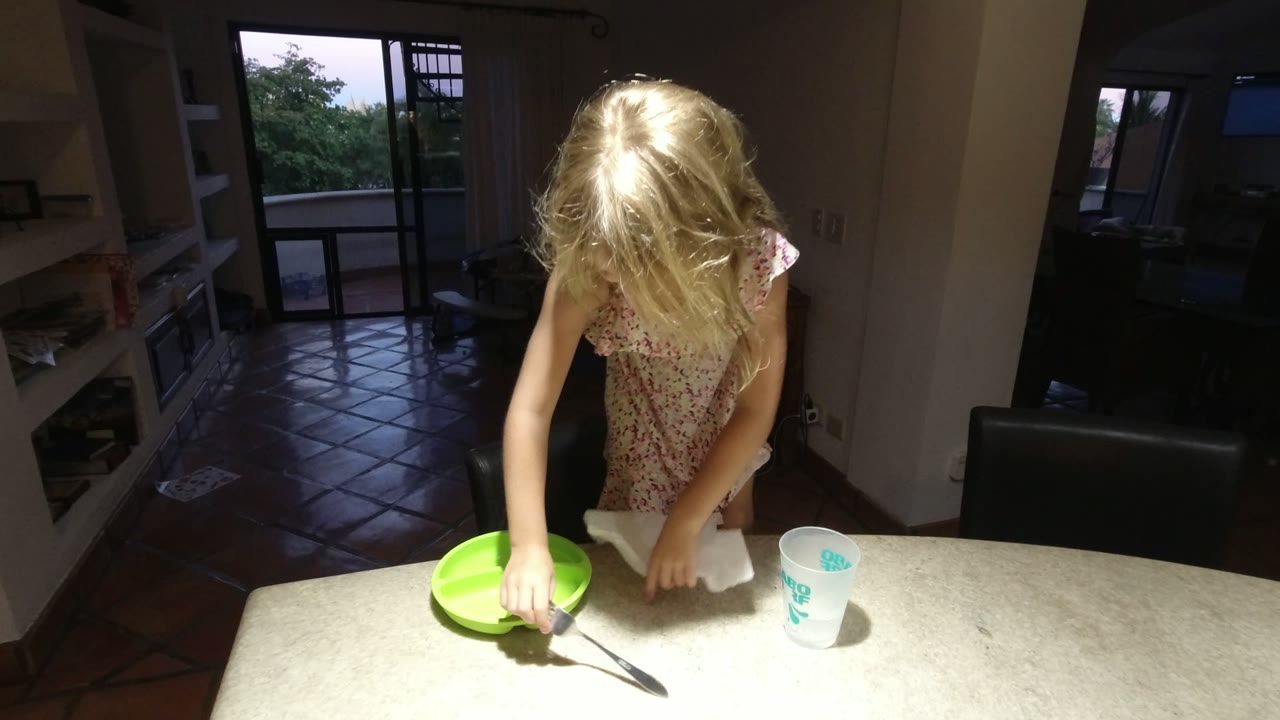 In Los Cabos, Mexico, the child reaches down near the green divided plate as the fork, napkin, and cup remain spread across the lit tabletop.