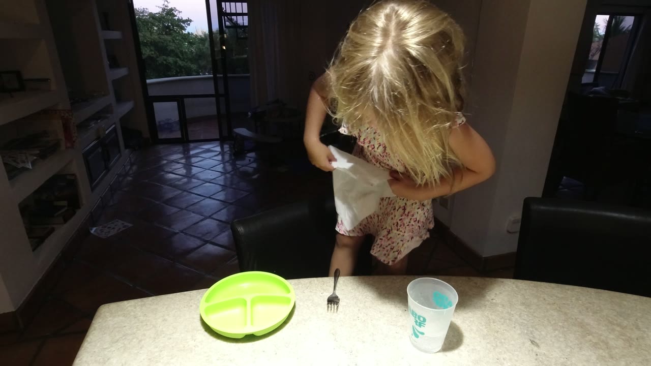 Blonde child or young woman holding a white cloth at a kitchen counter.