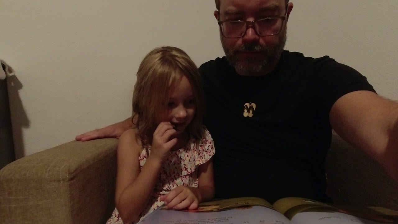 Father and young daughter seated on a sofa with an open book.