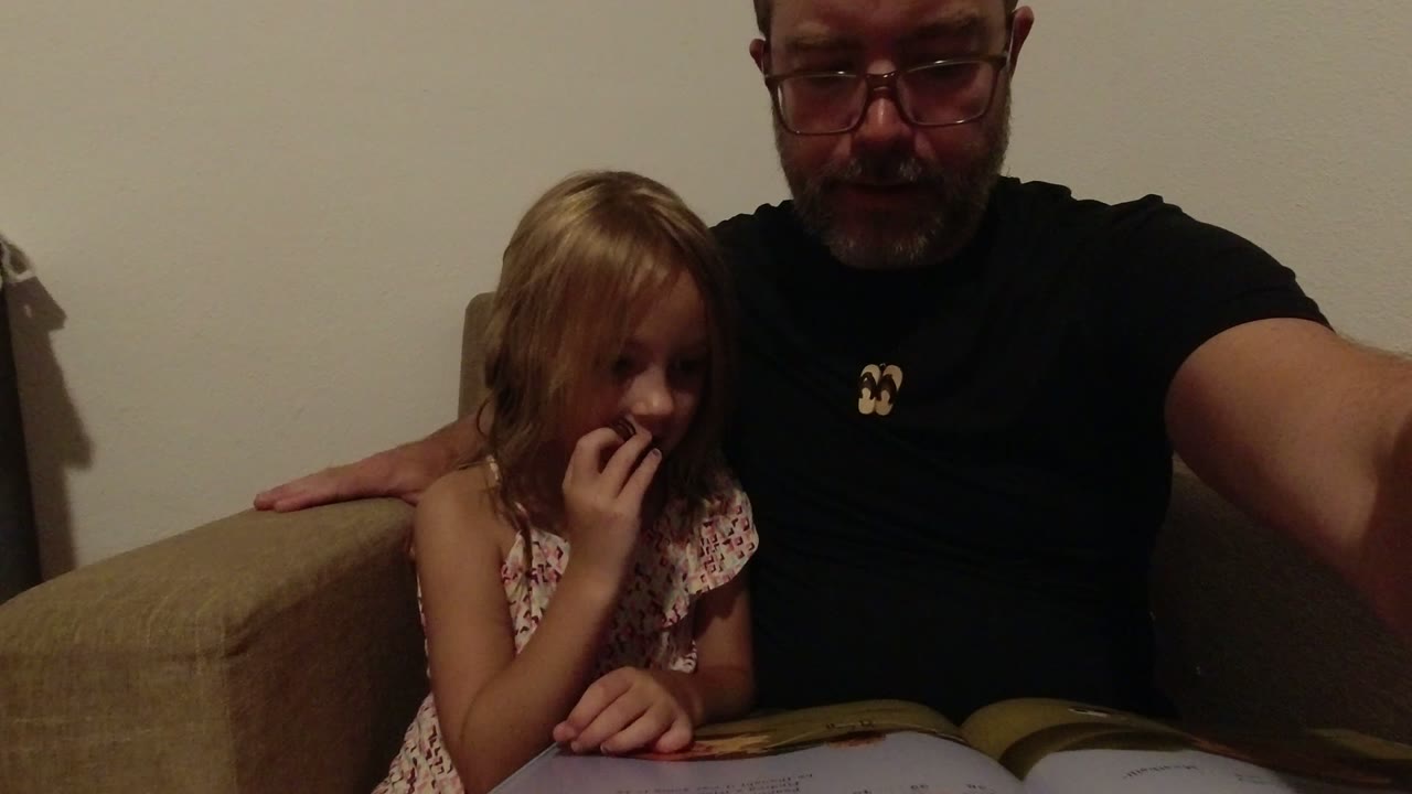 In Los Cabos, Mexico, the girl raises a finger near her mouth while her father remains beside her on the sofa with the open book visible below.