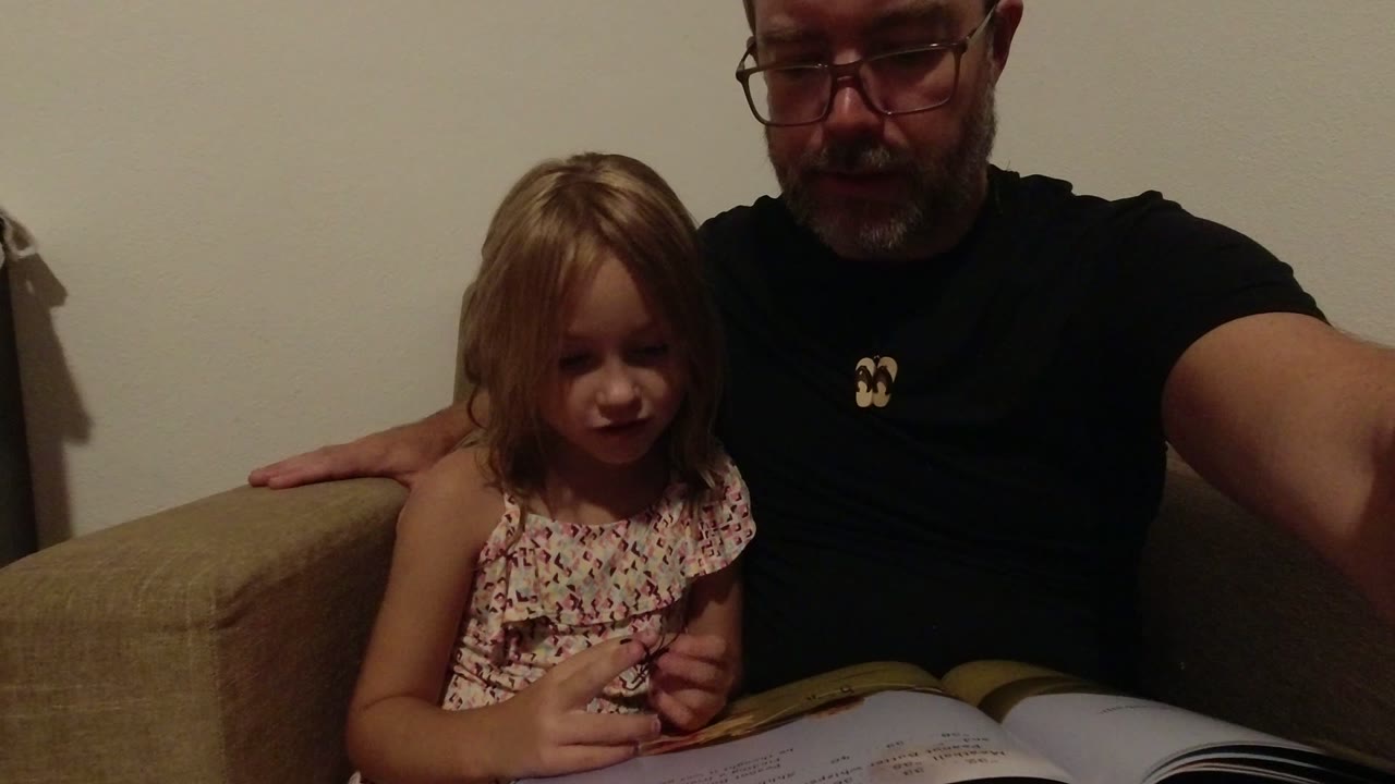 At the start of the Los Cabos clip, a young girl sits beside an adult man on a beige couch with an open book across their laps.