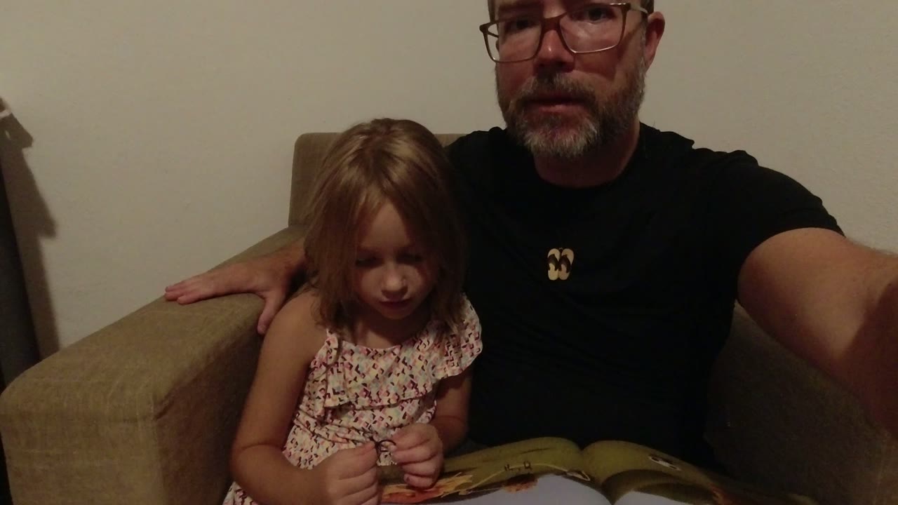 Father and young daughter seated with an open book in a beige chair.