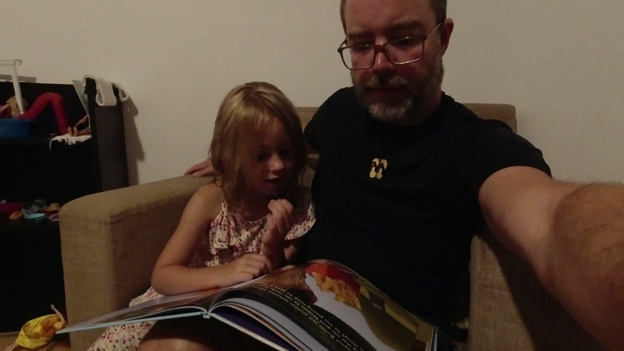 In Los Cabos, Mexico, the young girl turns toward the open book while her father remains beside her, partly cropped by the close self-recorded framing.