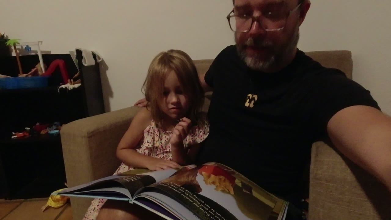 Young girl sits beside an adult man with an open magazine on her lap.
