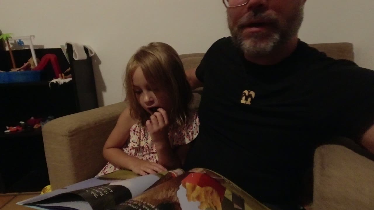 The girl looks down toward the open magazine while the adult man remains cropped on the right side of the warm indoor frame in Los Cabos, Mexico.