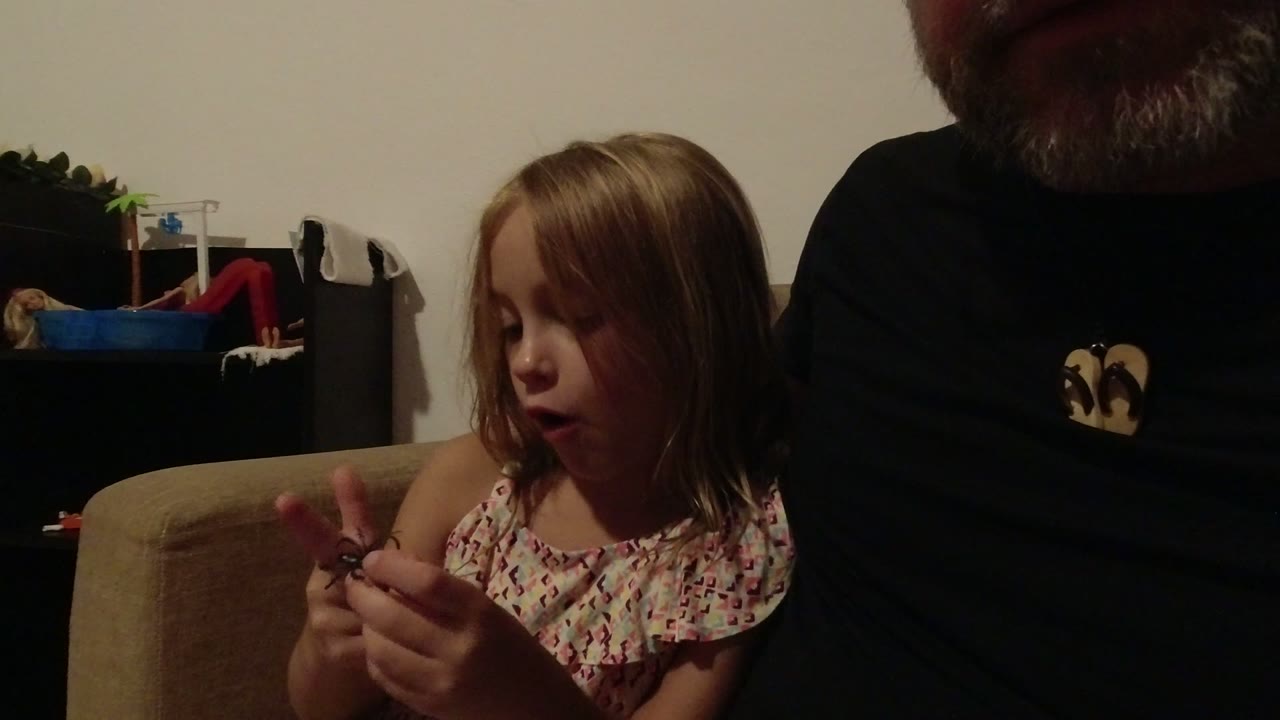 In Los Cabos, Mexico, a young girl sits on a beige couch beside a partially visible older man and looks down while holding a small dark object.