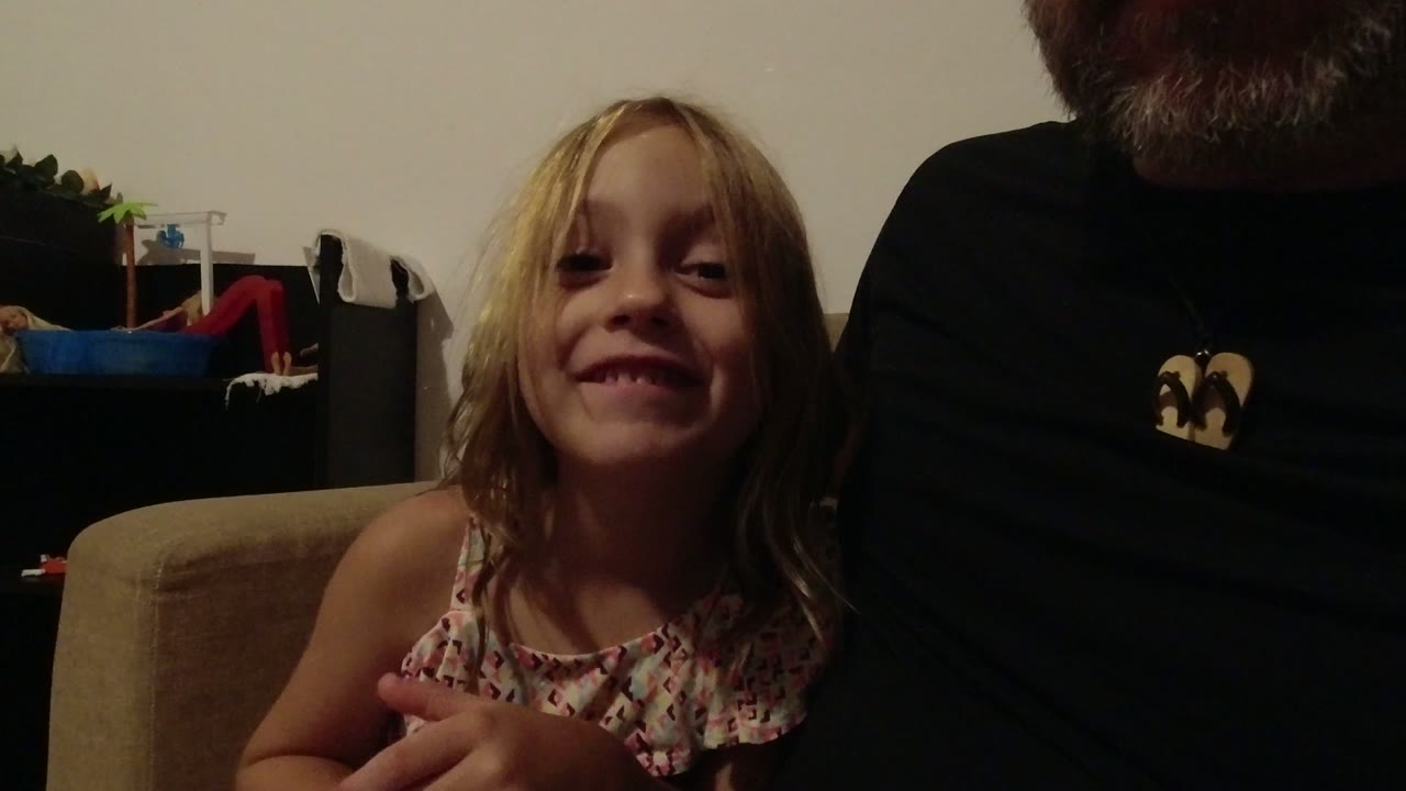 At 0:00, a young blonde girl smiles near the camera in a dim Los Cabos home interior while a bearded adult in a dark shirt is cropped beside her.
