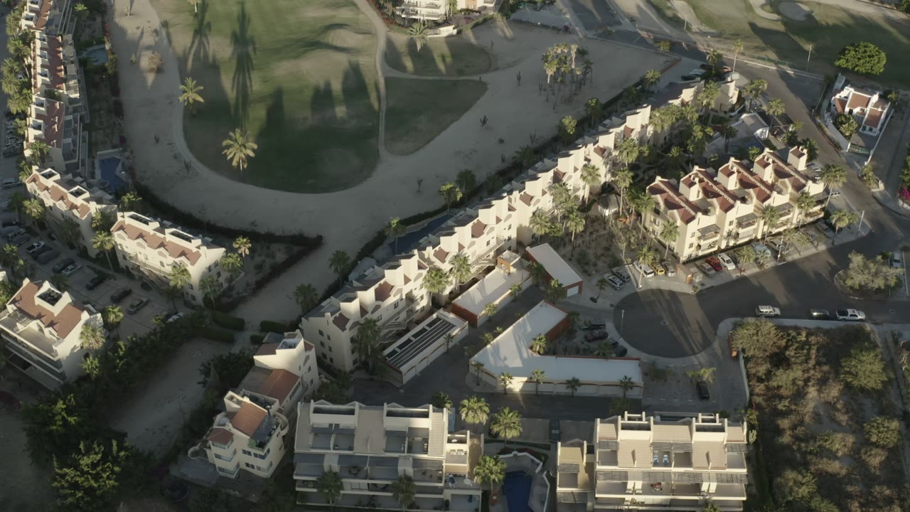 Overhead view of condominium buildings beside a golf course and palm-lined roads.