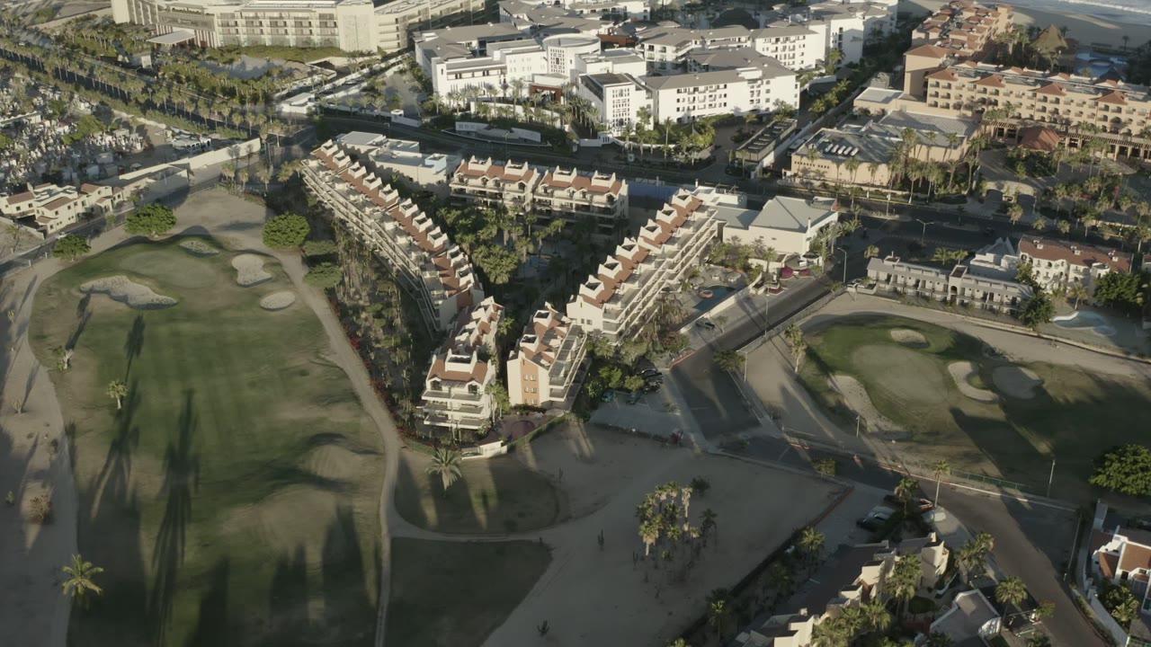 Aerial view across a golf course toward rows of red-roof buildings and larger white buildings.