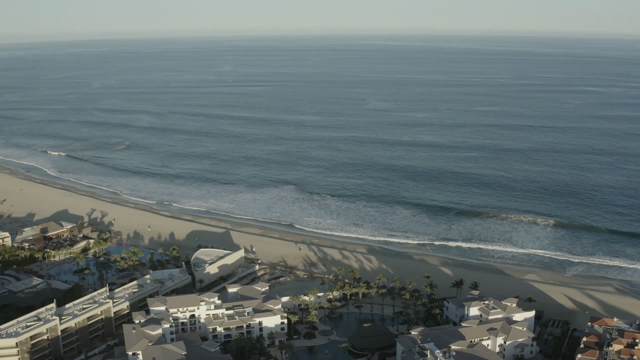 A second Los Cabos aerial frame shows the ocean occupying most of the view, with thin surf bands reaching the beach and no visible people on the sand.
