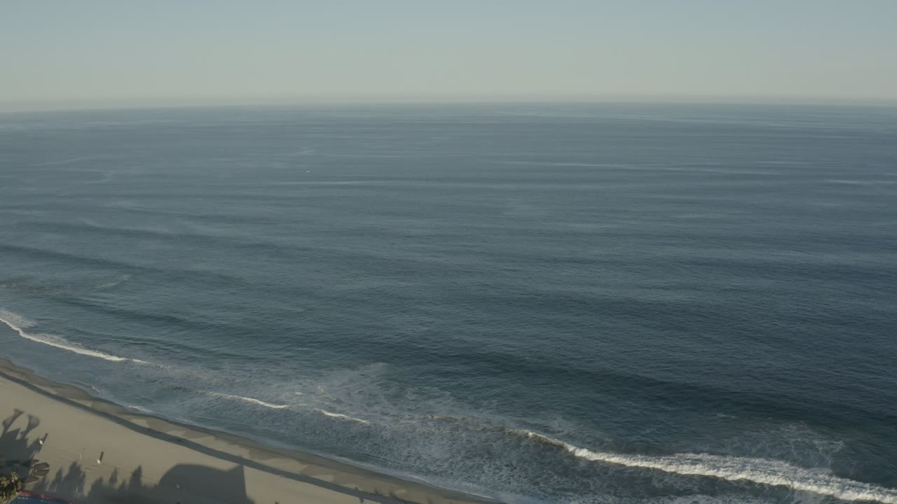 Wide aerial view of dark blue ocean waves reaching a sandy beach.