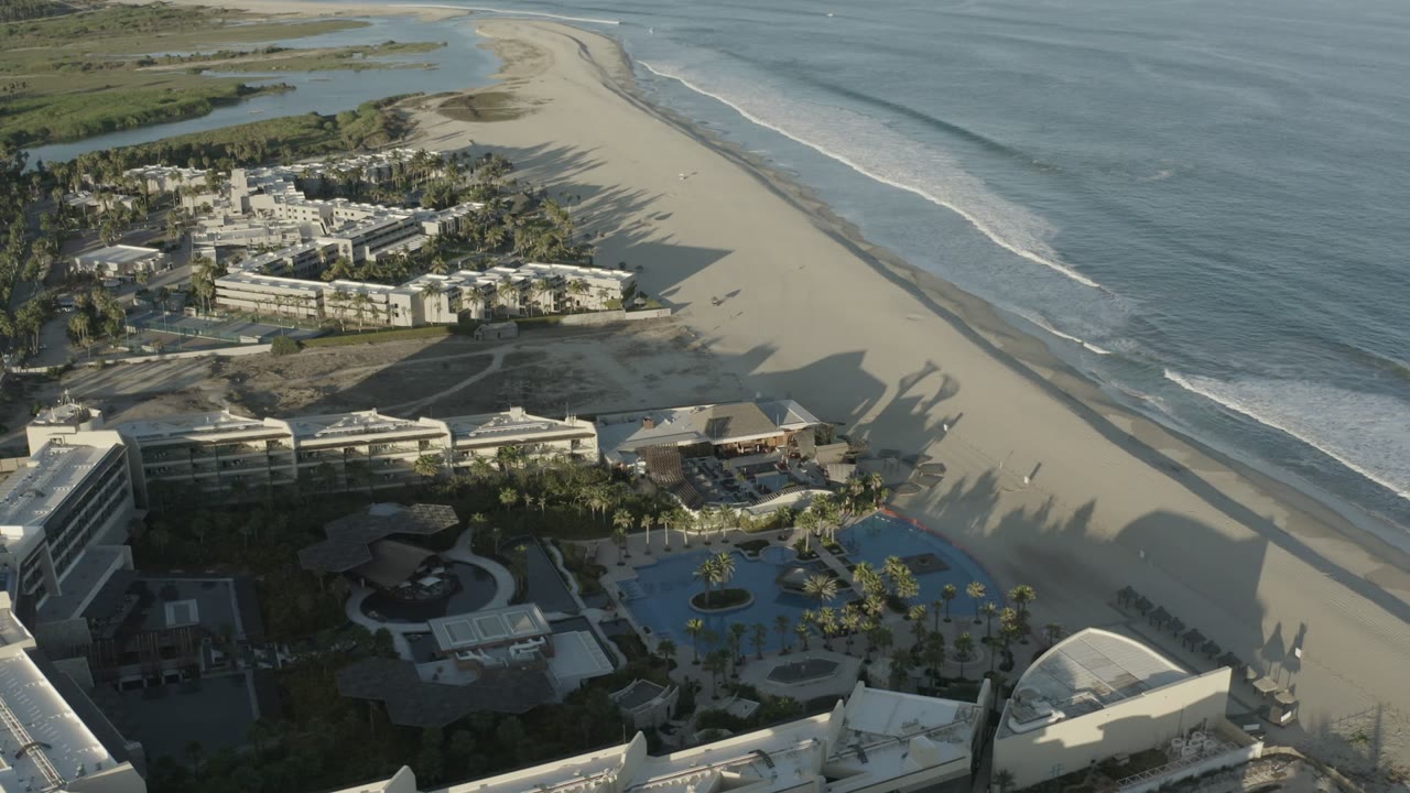 Aerial view of beachfront buildings, pools, sand, and ocean surf.