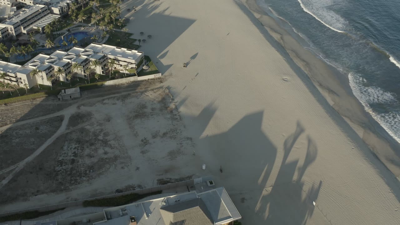 Aerial view of hotel buildings beside a sandy beach and ocean surf.