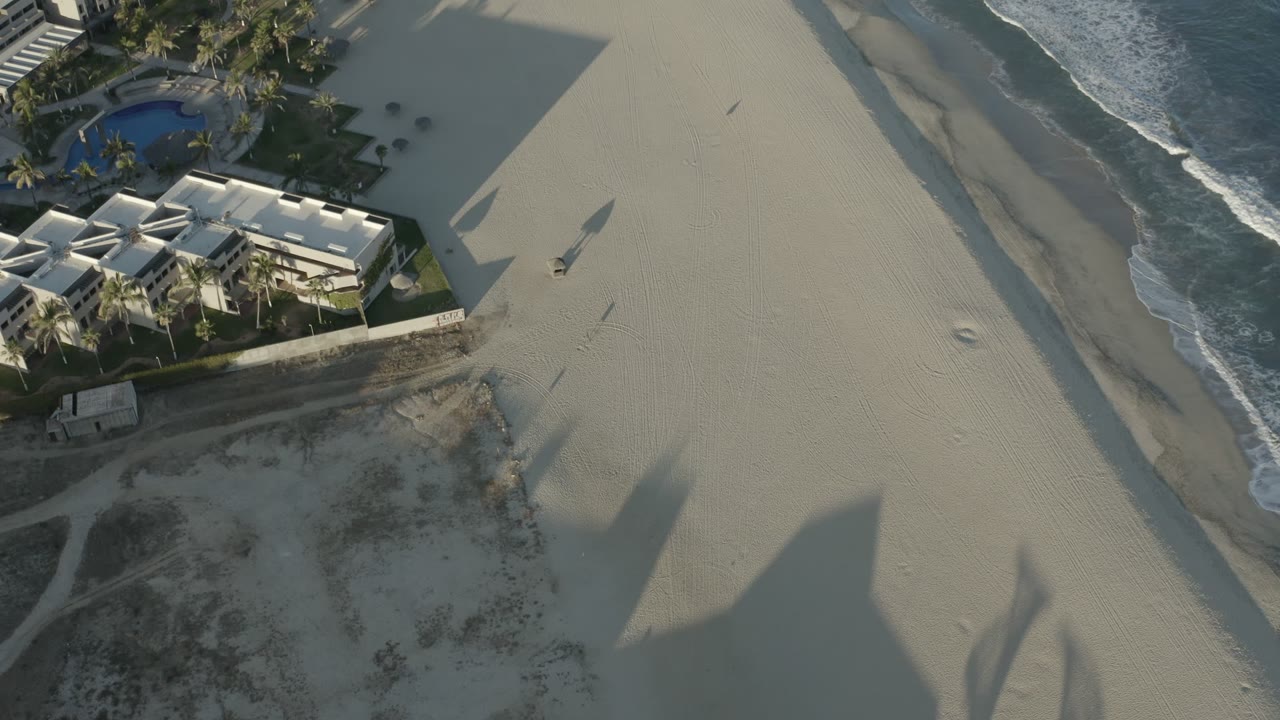 Aerial view of empty beach beside beachfront apartments and surf.