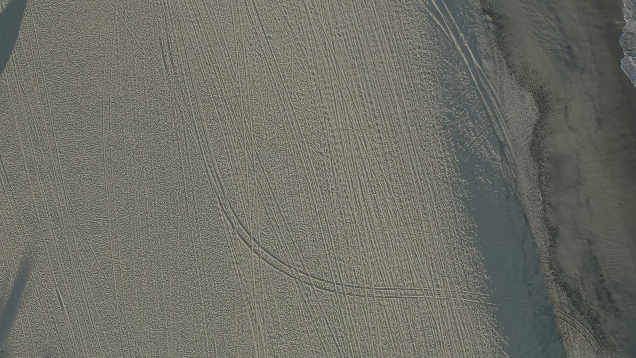 Overhead view of rippled sand and a darker vertical channel.