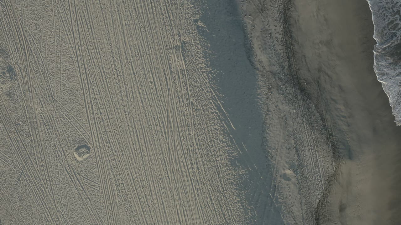 Overhead shoreline with foam, wet sand, and parallel beach tracks