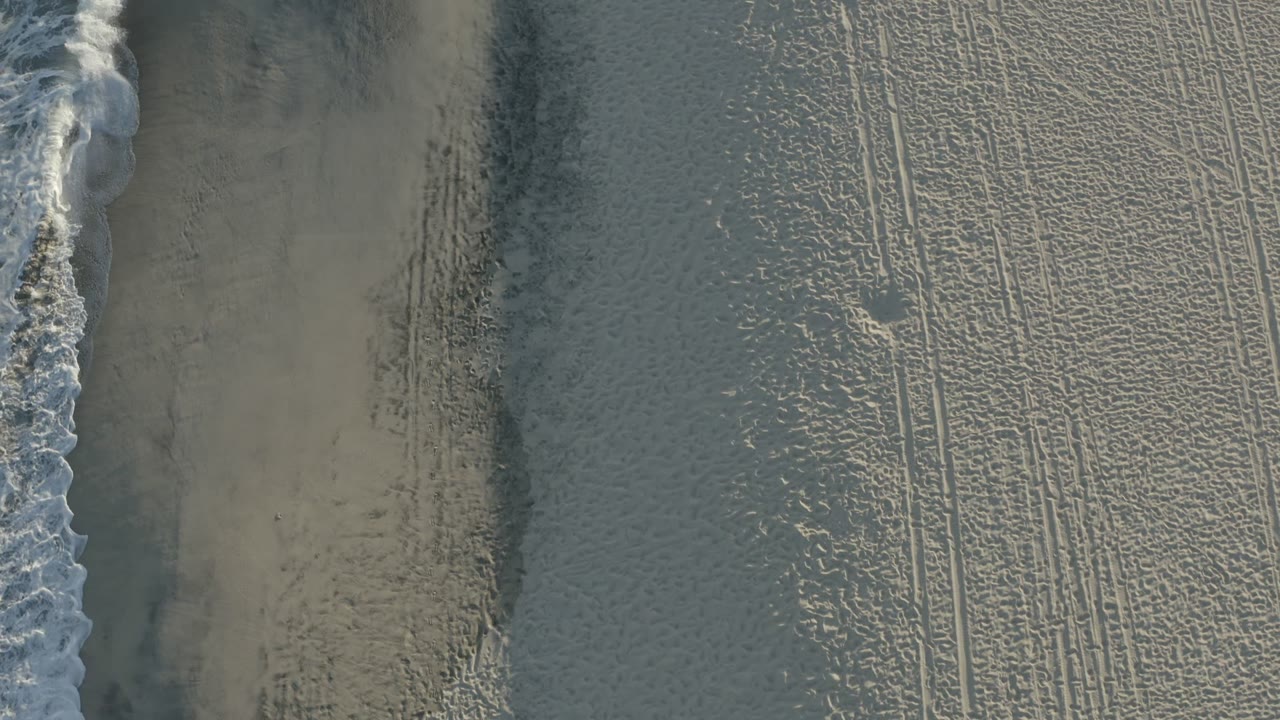 Top-down beach with surf foam and marked sand