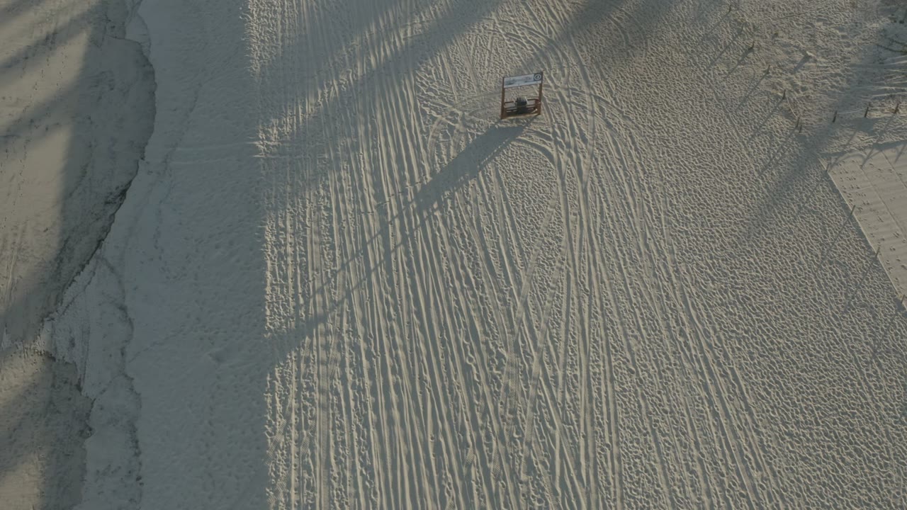 Aerial view in Los Cabos, Mexico with textured white sand, a small rectangular beach structure near the top of frame, and no visible people.