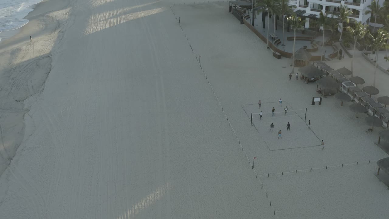 High aerial view of beach, surf, beachfront buildings, and a volleyball court.