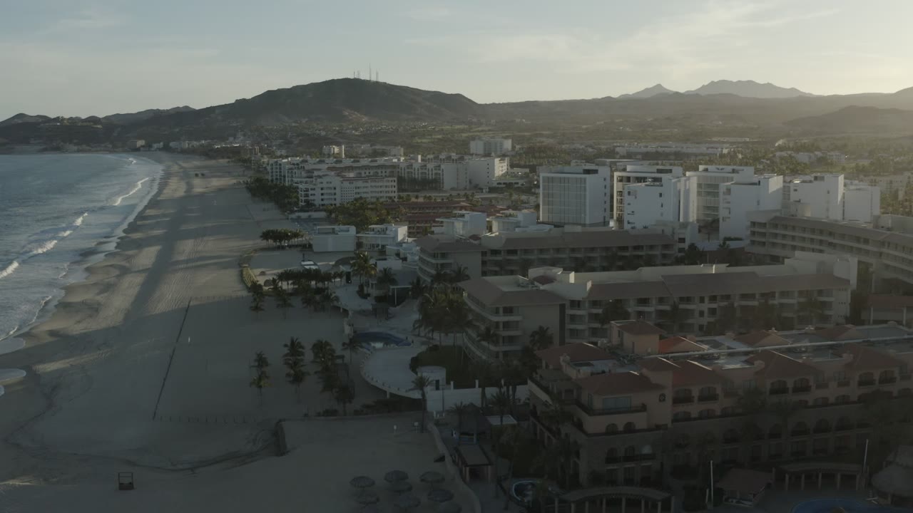 Aerial view of beach, surf, hotel buildings, and mountains.