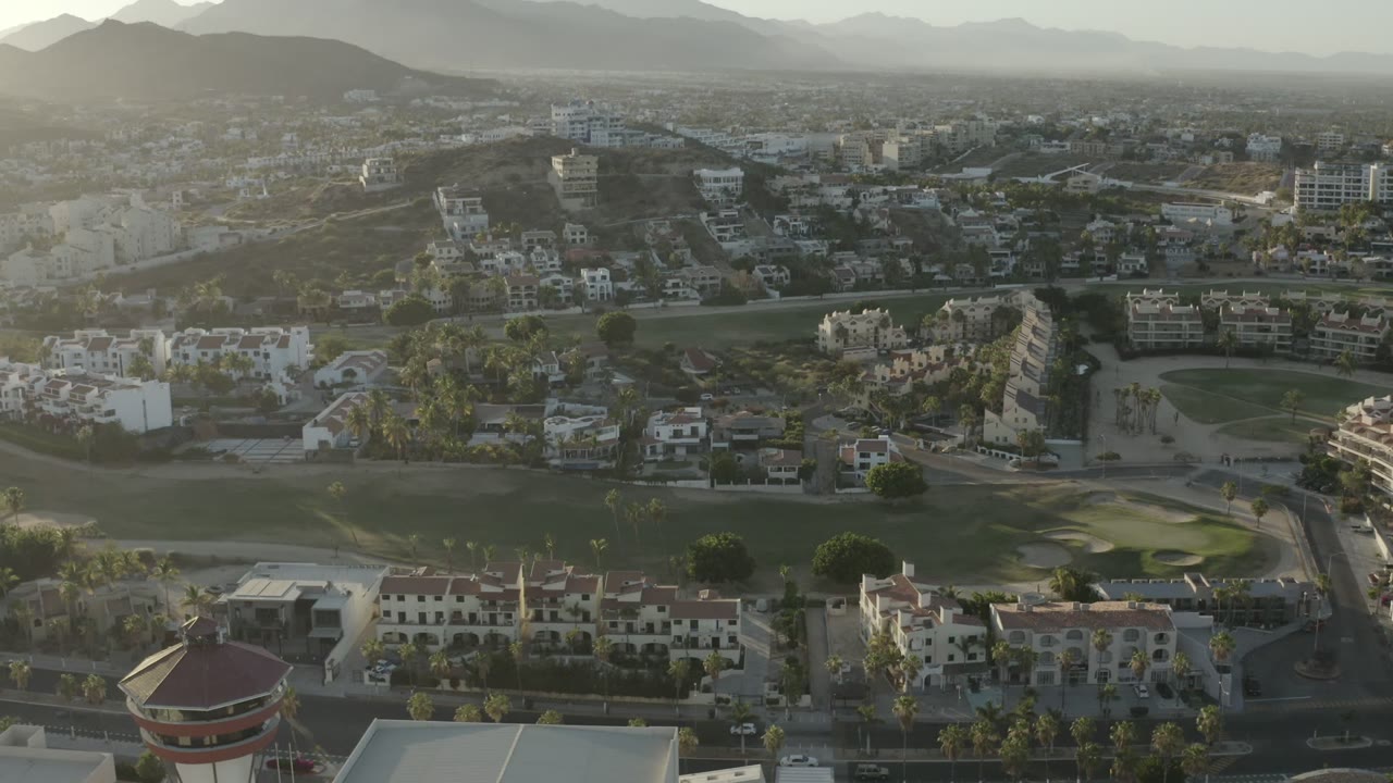 Aerial view of homes, streets, golf greens, and distant hills.