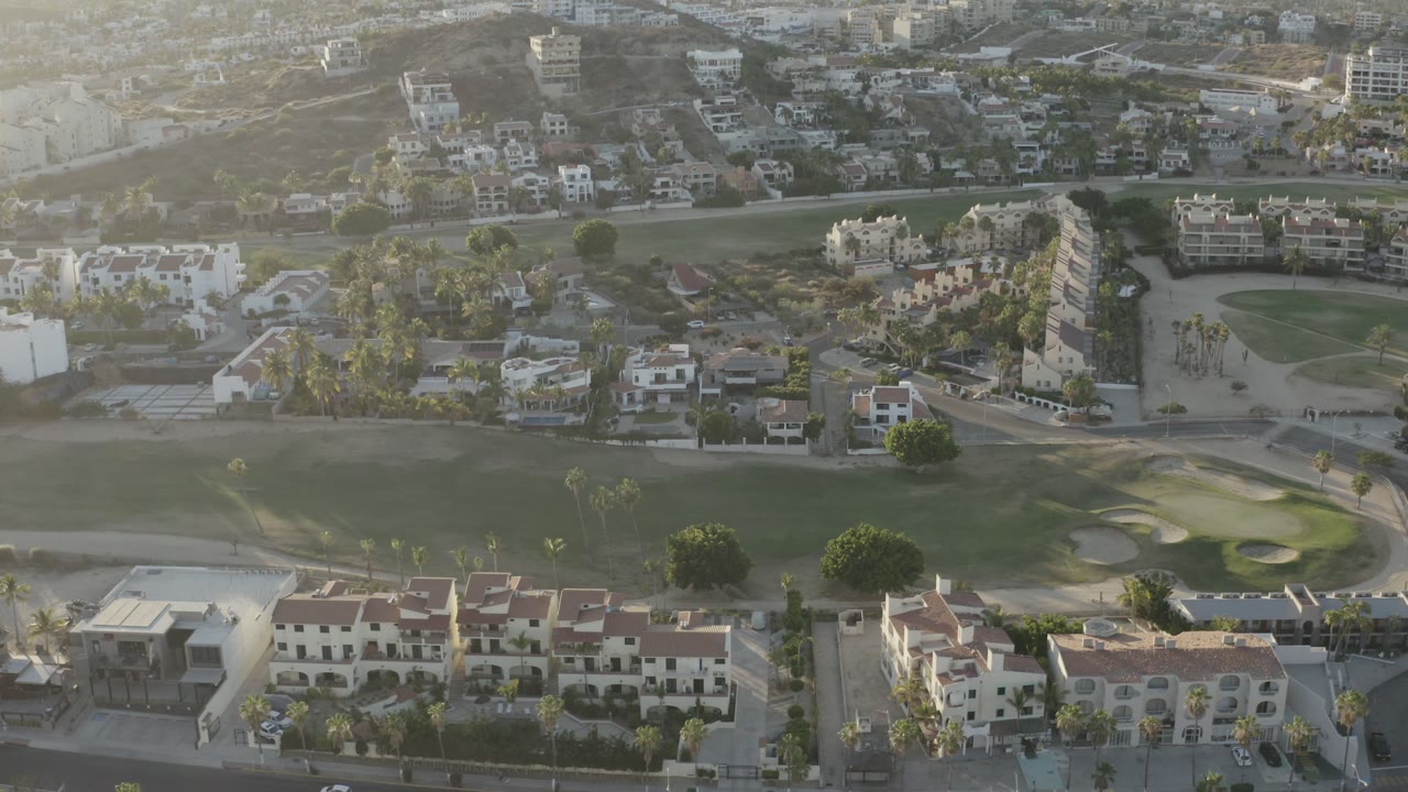 Drone view over hotel buildings, golf greens, sand bunkers, and a road.